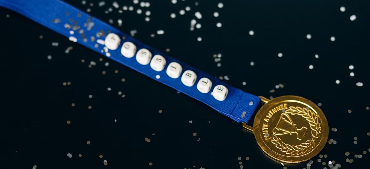 Close-up of a gold medal on a blue ribbon with 'possible' beading, symbolizing achievement.